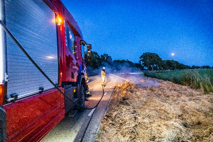 Brandweer blust broei in stro langs weg in Nijeveen